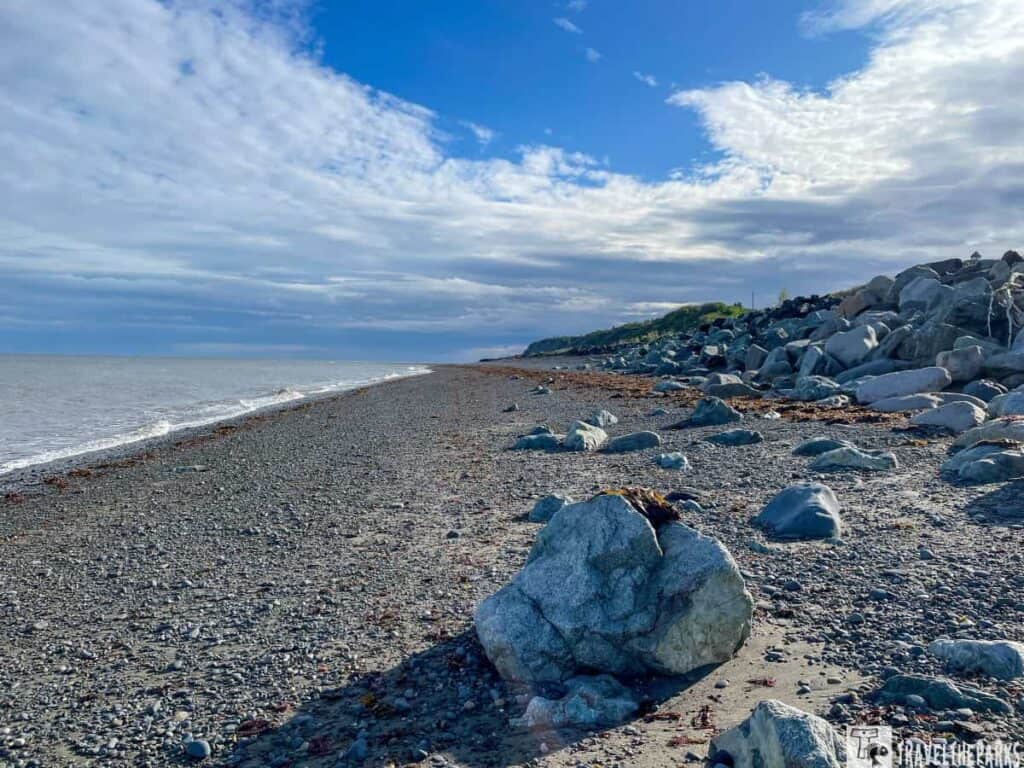 Rocky beach along the road to Homer, Alaska, with ocean waves and a partly cloudy sky.