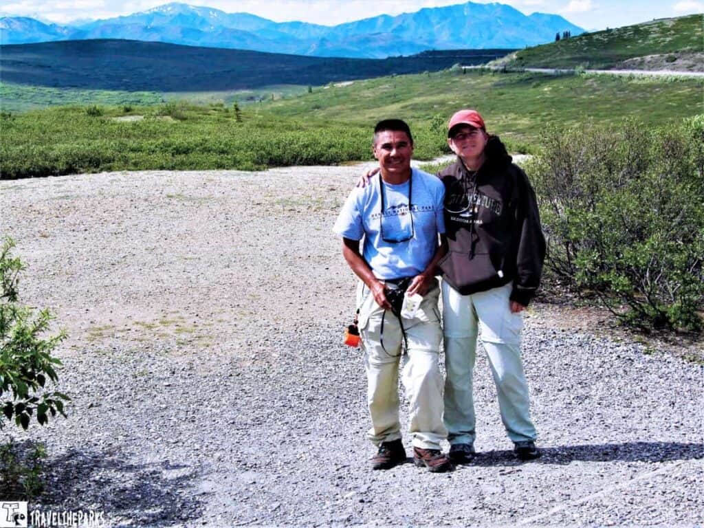 Two people standing on a gravel path at Primrose Ridge in Denali National Park in front of a mountain backdrop.