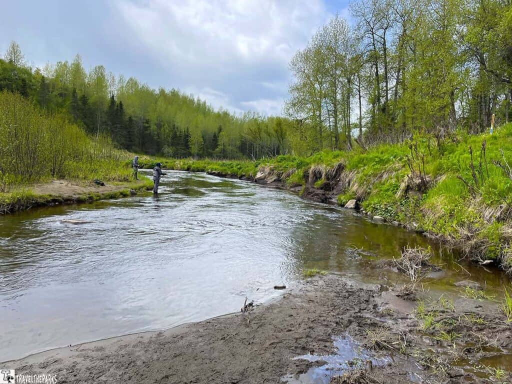Ninilchik river surrounded by greenery with two people fishing under an overcast sky.