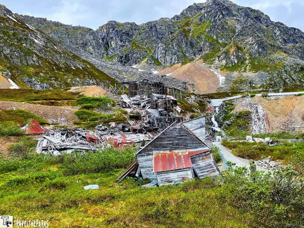 Ruins of wooden mining structures amidst a mountainous landscape with greenery at Independence Mine State Historical Park.

