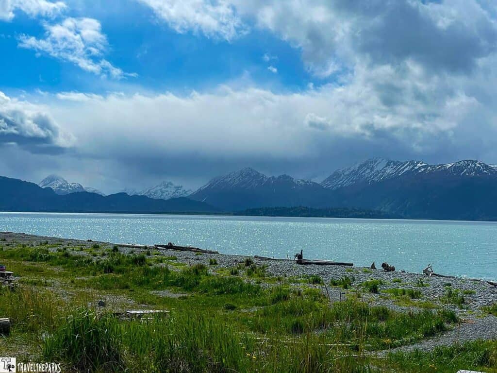 A tranquil waterscape Kachemak Bay with snow-capped mountains in the background and a cloudy sky above.