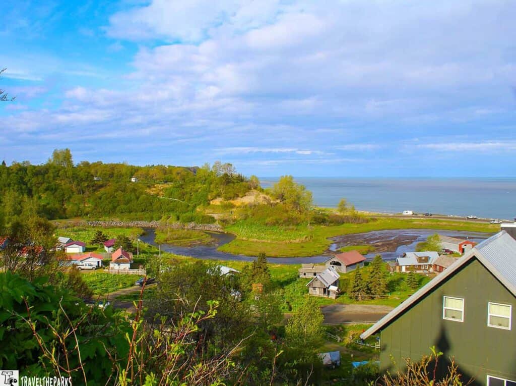 Scenic view of the Ninilchik coastal town with homes, a river, and the ocean in the background under a cloudy sky.
