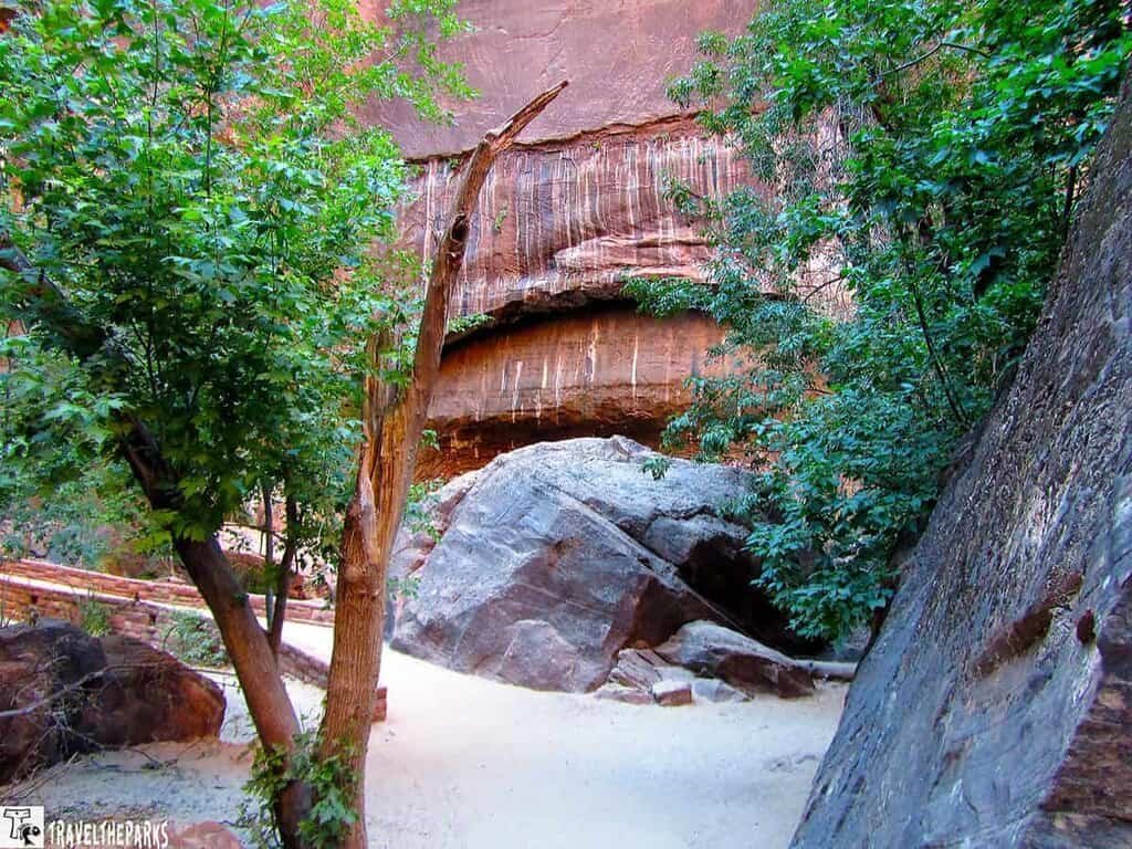 Rocky landscape with a boulder, trees, and a reddish-brown rock formation.