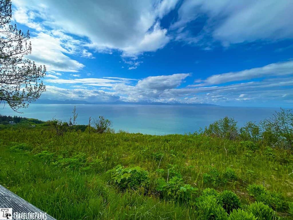 Scenic view of a grassy field leading to a calm body of water under a blue sky with clouds.