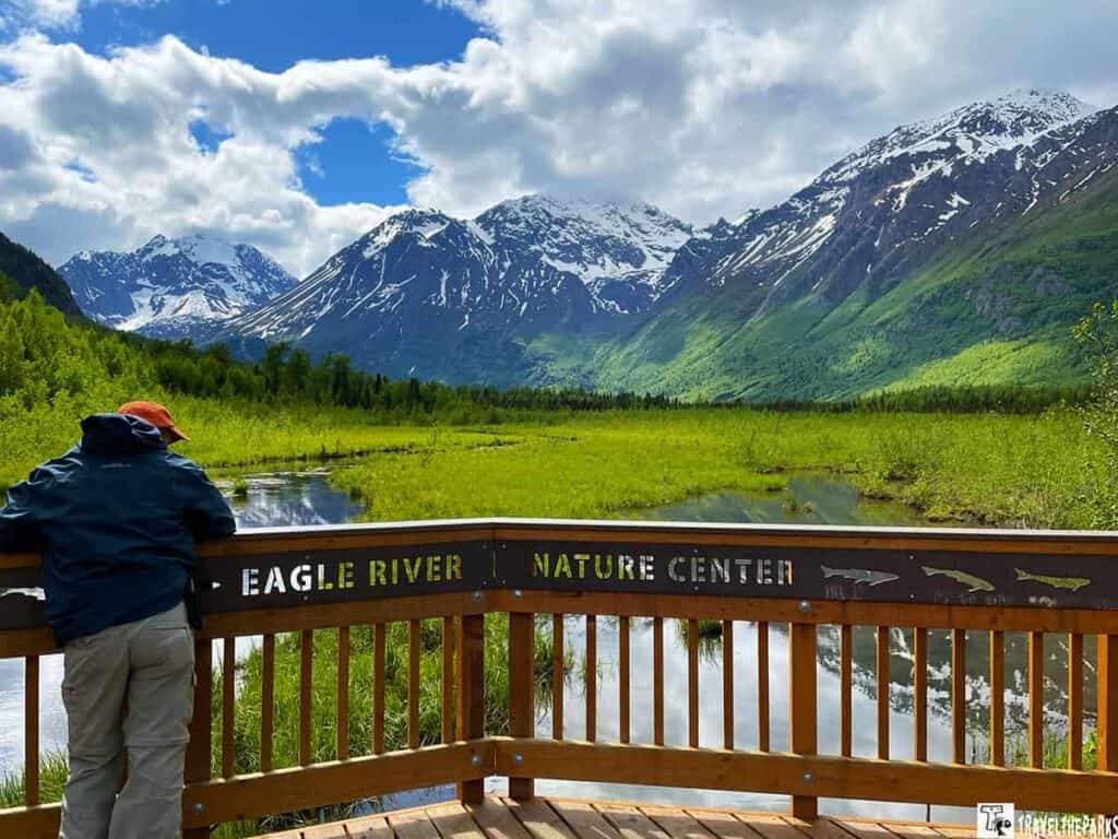 Person leaning on a railing at Eagle River Nature Center with mountains and greenery in the background.

