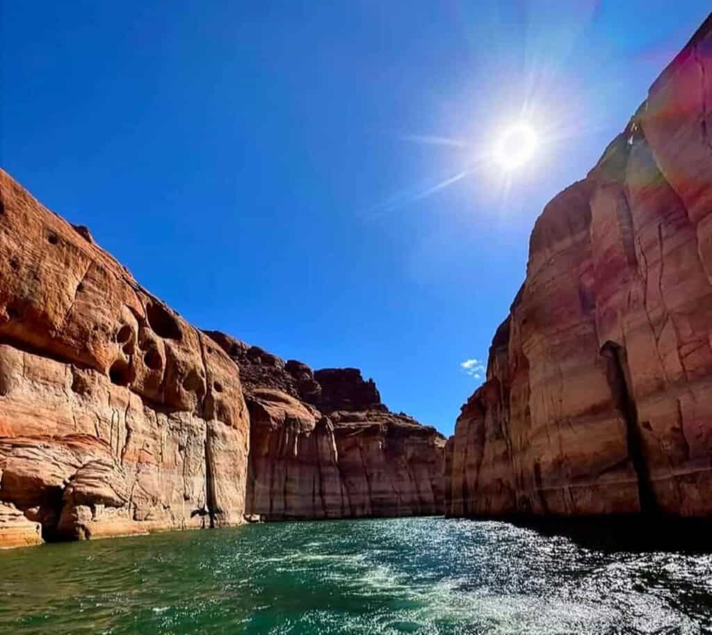 Canyon walls and Lake Powell under a clear blue sky and bright sun.