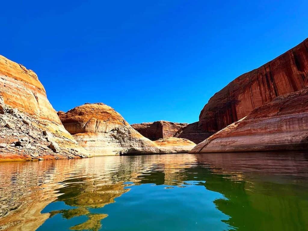 Scenic view of Lake Powell with vibrant rock formations and reflective water under a clear blue sky.