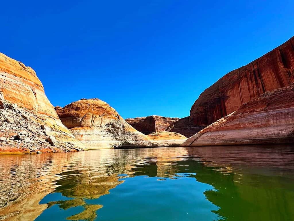 Scenic view of Lake Powell with vibrant rock formations and reflective water under a clear blue sky.