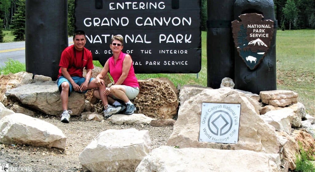 Two people sitting in front of a Grand Canyon National Park sign.