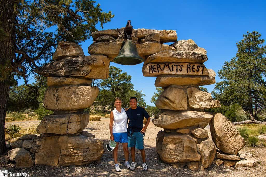 Two people standing under a stone arch labeled "HERMIT'S REST" with a bell on top.