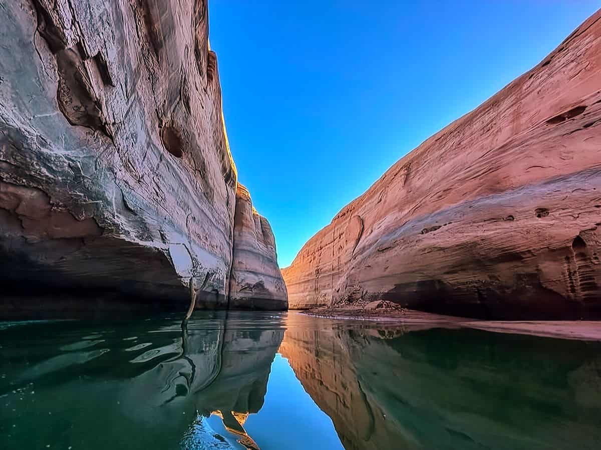 A narrow canyon at Lake Powell with reflecting water, under a clear blue sky.