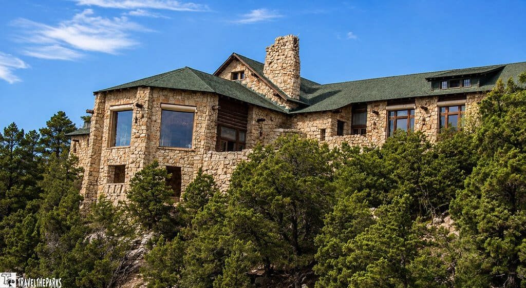 Grand Canyon Lodge: Stone building with green roof and large windows perched on a cliff, surrounded by lush greenery under a bright blue sky, exuding a serene and rustic charm.