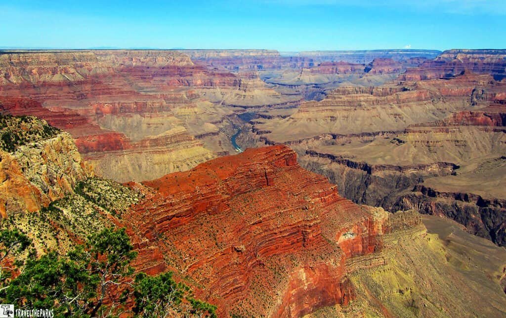 Panoramic view of the Grand Canyon from Hermit's Rest, featuring layered rock formations in shades of red and brown, with a river winding through the canyon.