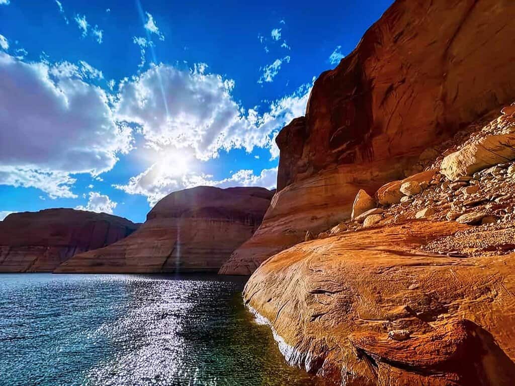 Scenic view of Lake Powell in Arizona with sandstone cliffs, blue sky, and glistening water.