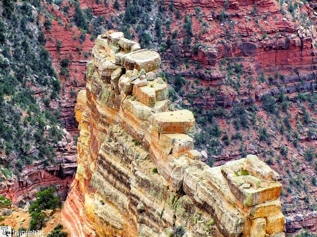 Tritle-Peak-Roosevelt-Point: A rugged cliff edge at the Grand Canyon, with layered rock formations and sparse green vegetation. The background shows steep, red rocky walls, conveying a sense of vastness and natural beauty.