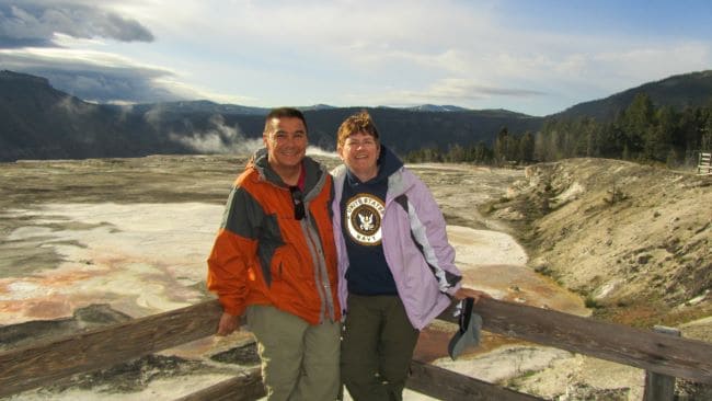 Two people on a deck overlooking Mammoth Hot Springs with mountains in the background.