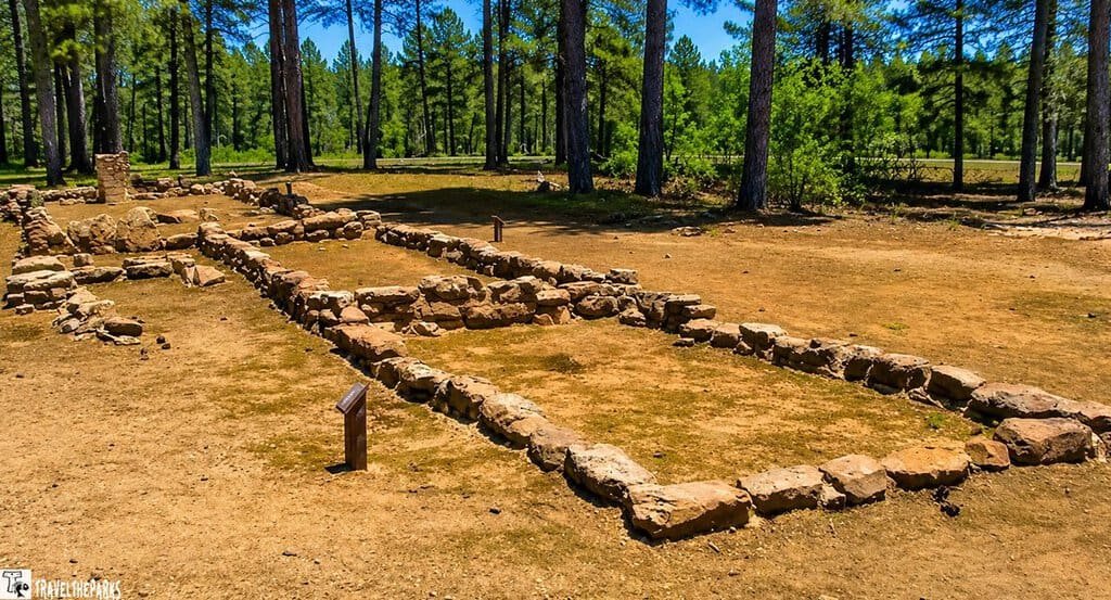 Walhalla Glades-Ancient Ruins: Ancient stone ruins form a rectangular outline on dusty ground, surrounded by trees. The scene evokes history and a sense of mystery.