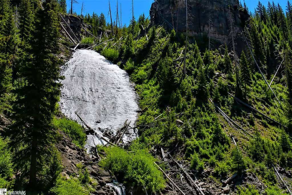 Wraith Falls cascades down rocky cliffs, framed by lush trees and majestic mountains in the background.