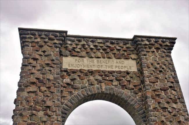 Top section of the Roosevelt Arch with a stone inscription against an overcast sky.

