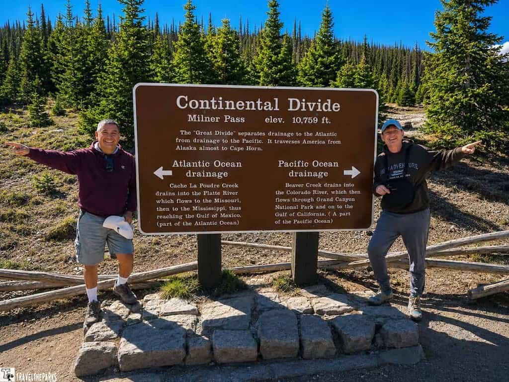  Milner's Pass Two people stand beside a sign indicating the Continental Divide in Rocky Mountain National Park, surrounded by scenic landscapes.
