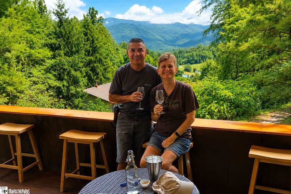 Two people sitting on a balcony with a view of the Great Smoky Mountains and surrounding greenery.