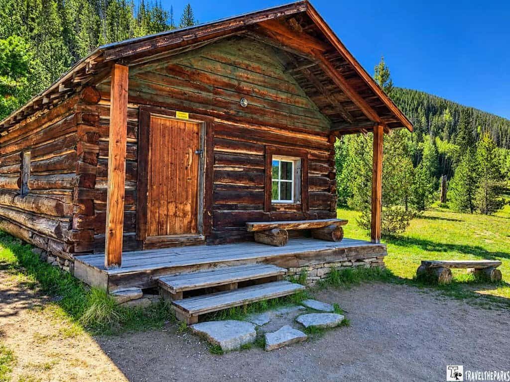  Holzwarth Historic Site a rustic log cabin located in a field, framed by the stunning landscape of Rocky Mountain National Park.