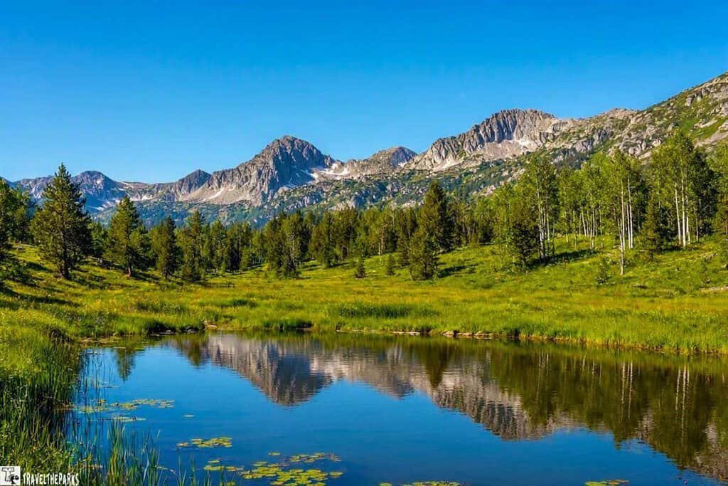 Beautiful mountains reflected in a still pond, nestled in a green field, creating a peaceful natural landscape.