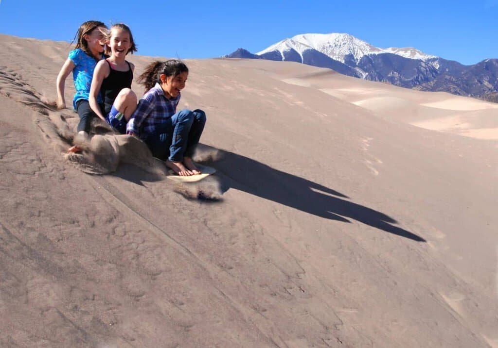 Three girls use a specially designed sand sled (available for rent) to slide quickly down the dunes.