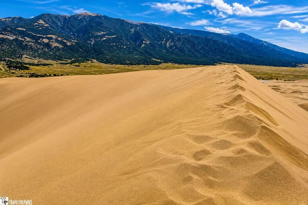 A large sand dune with footprints against a backdrop of mountains and clouds at Great Sand Dunes National Park