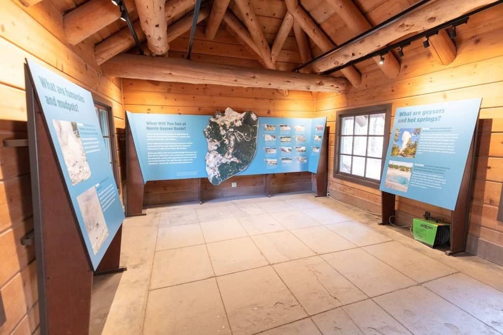 Interior of Norris Geyser Basin visitor center showing wood walls and informative panels about geothermal features, including a map and photographs.