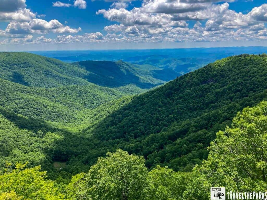 Lush green mountains and valleys under a blue sky with clouds.