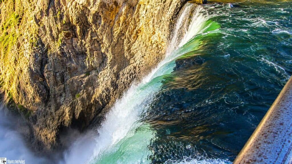 Close-up of a waterfall flowing over jagged rock formations in the Grand Canyon of Yellowstone, with dark, turbulent water transitioning to turquoise at the edge.