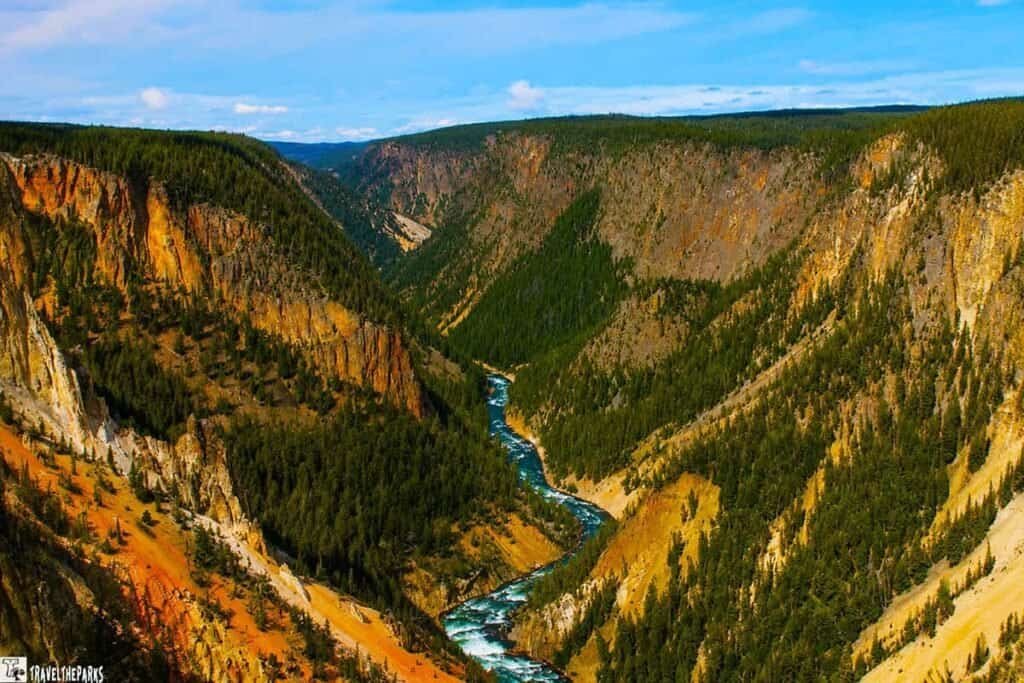 Aerial view of a colorful canyon with rugged cliffs, a winding turquoise river, and dense forests under a blue sky.