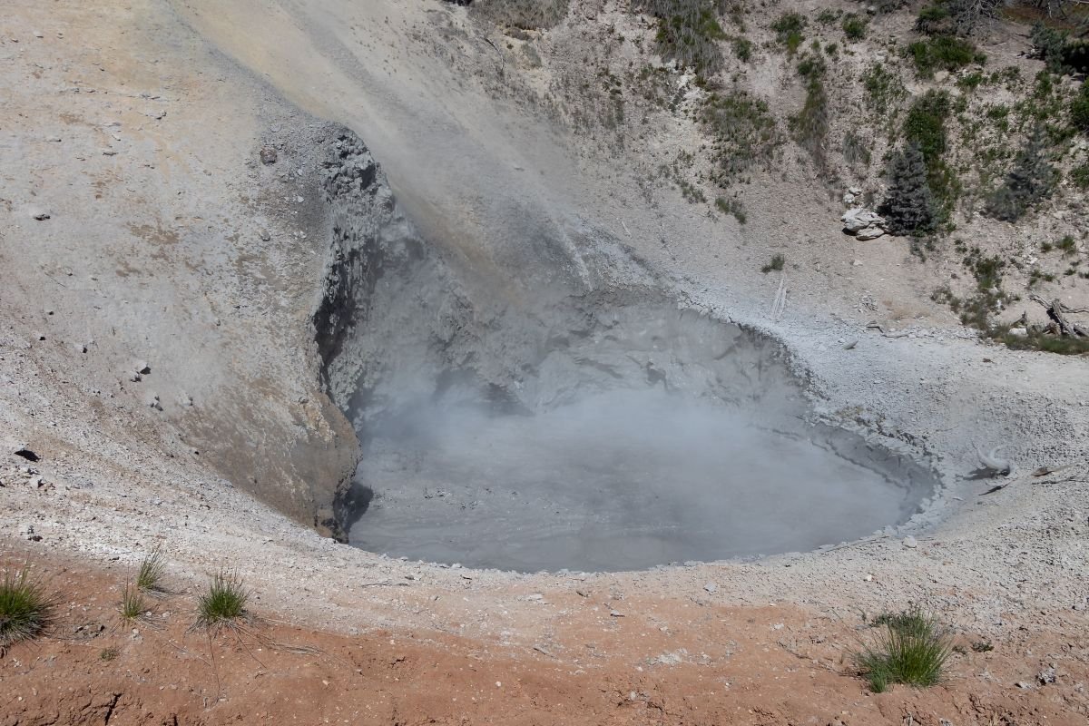 A close-up of a mud volcano in Yellowstone's Hayden Valley, with steam rising from a large, active hole.