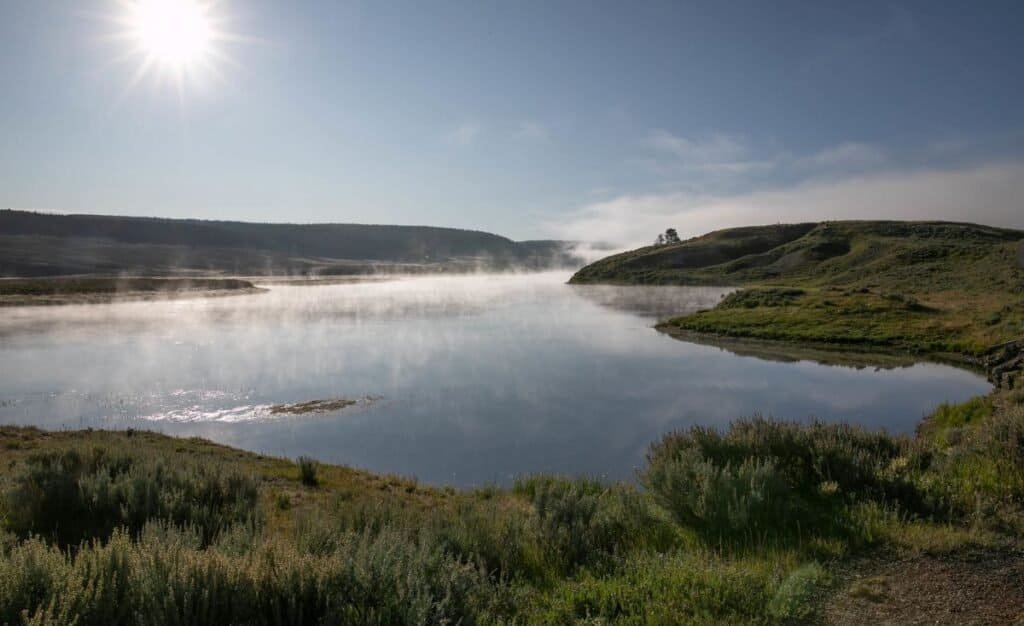 Sunlight glimmers on the Yellowstone River in Hayden Valley, with mountains rising majestically in the background.