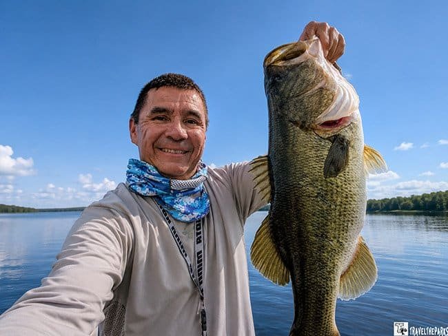Big Bass-Big Cypress Preserve: Person holding a large fish with a bright sky in the background.