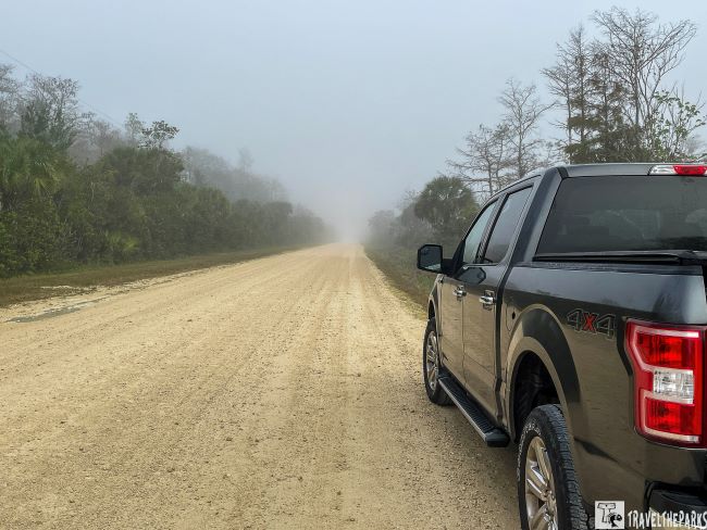 A black pickup truck parked on the side of a foggy dirt road surrounded by trees.