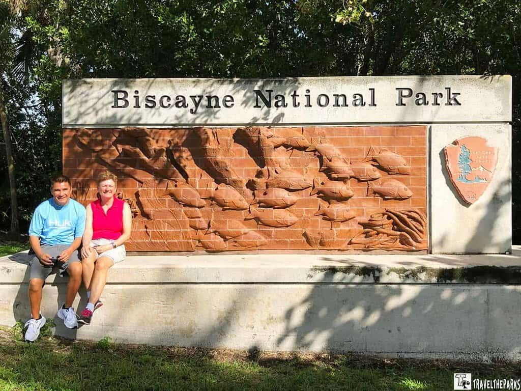 Biscayne National Park entrance sign featuring fish carvings with two people seated in front.