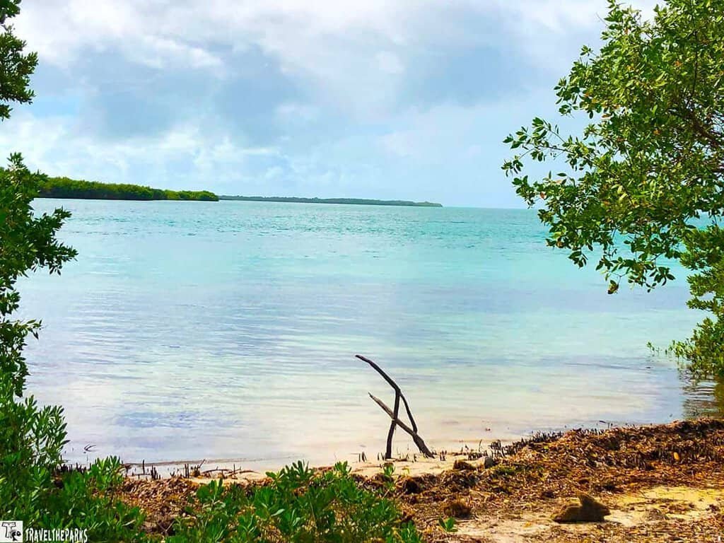 Biscayne National Park: A calm beach scene with turquoise water, sandy shore, and surrounding greenery under a partly cloudy sky.