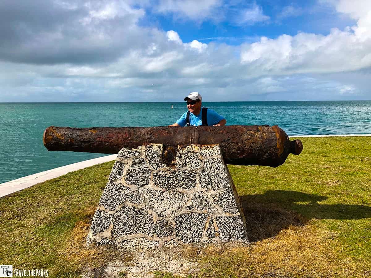 Boca Chita Key: Rusted cannon on a stone base by the sea with a person standing behind it.
