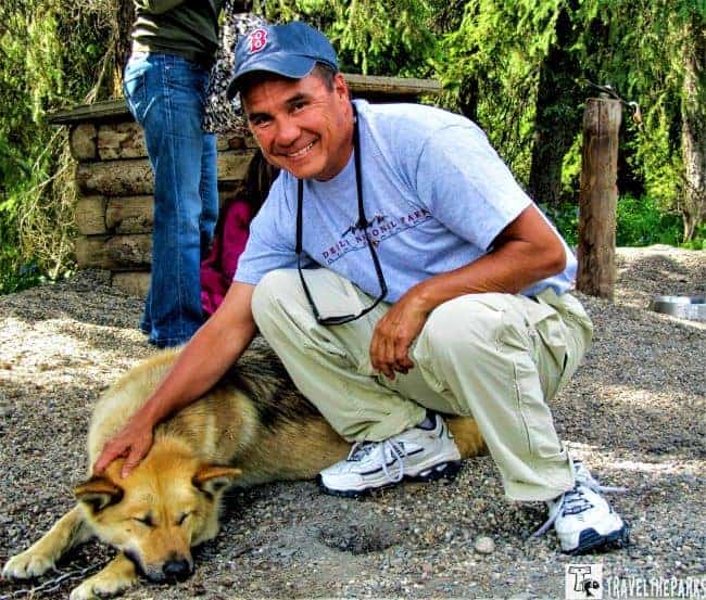 Person petting a brown dog on a gravel path in a forested area.

