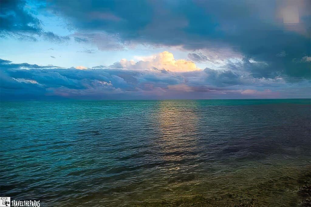 A Florida Nature Coast seascape with dark clouds overhead and sunlight illuminating patches of the ocean and clouds.