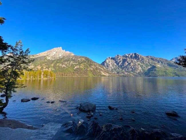 View of Jenny Lake with the Teton Range in the background under a clear blue sky.