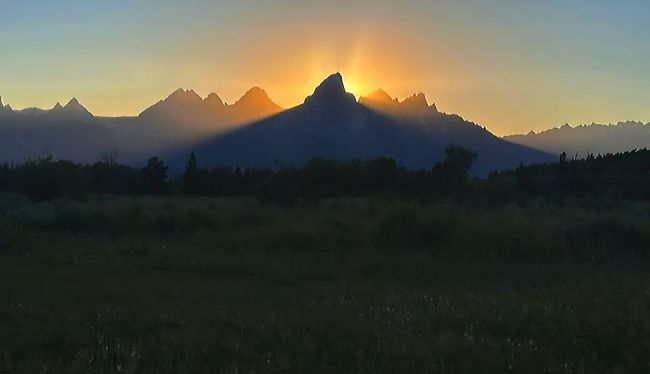 Silhouetted Teton mountain at sunset with sun rays creating a halo effect.