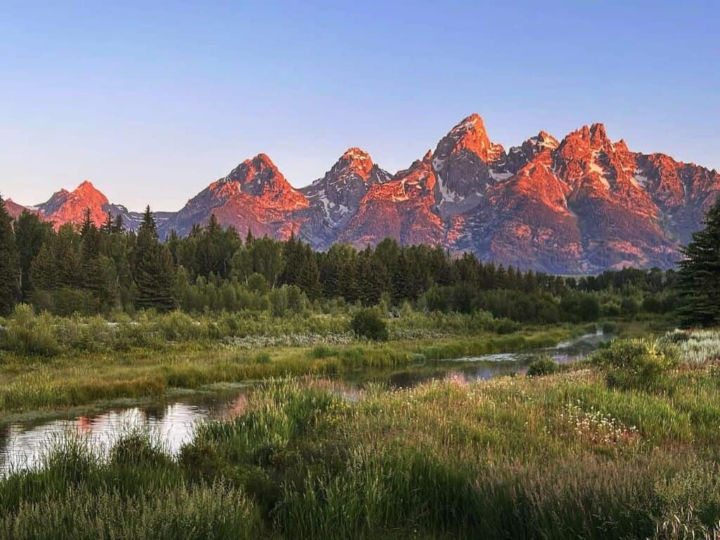 Grand Teton mountains at sunrise with forest and water in foreground. R. Crouse