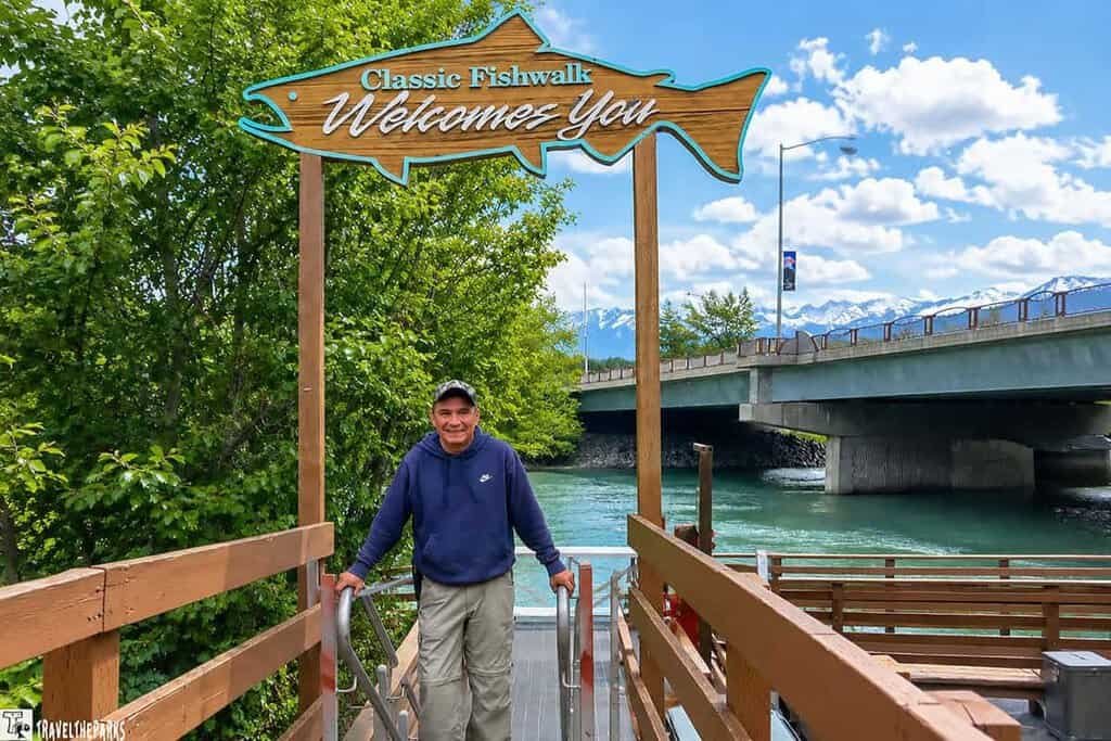 Man at the River Walk Soldotna. A welcome sign for the classic fish walk is above the boardwalk.