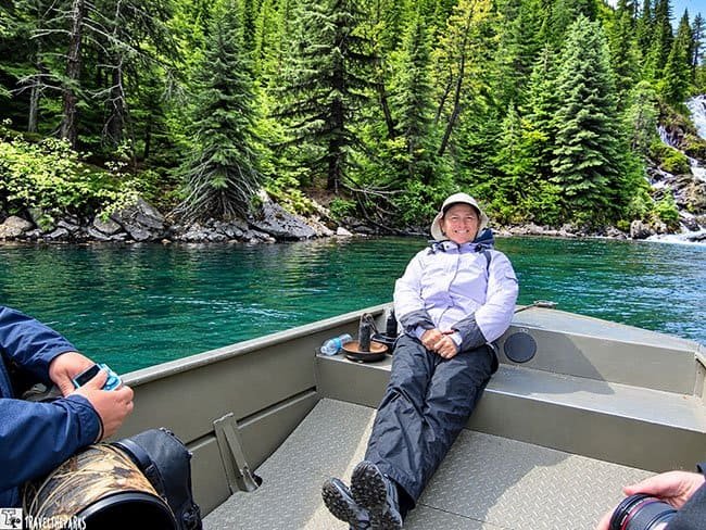 Bear Viewing Wolverine creek: Person relaxing on a boat on a river with green foliage in the background.