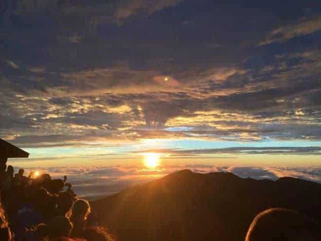 Sunrise over Haleakala with a crowd silhouetted in the foreground and mountains in the distance.