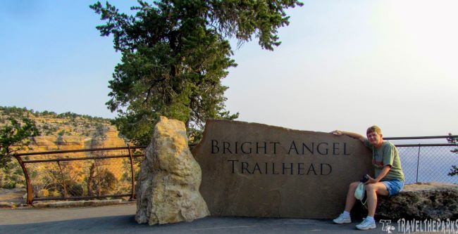 Person sitting next to the Bright Angel Trailhead stone sign.