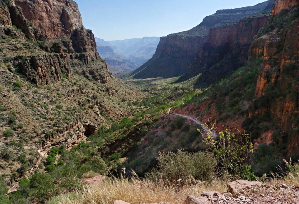 View of the Bright Angel Trail in the Grand Canyon, showing steep cliffs and a winding path under a blue sky.